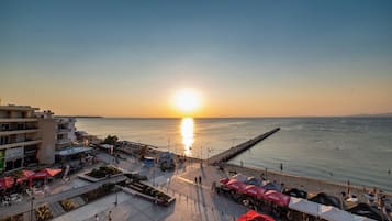 Un paseo marítimo con vistas al atardecer, mesas al aire libre y zona de restaurantes frente al agua.
