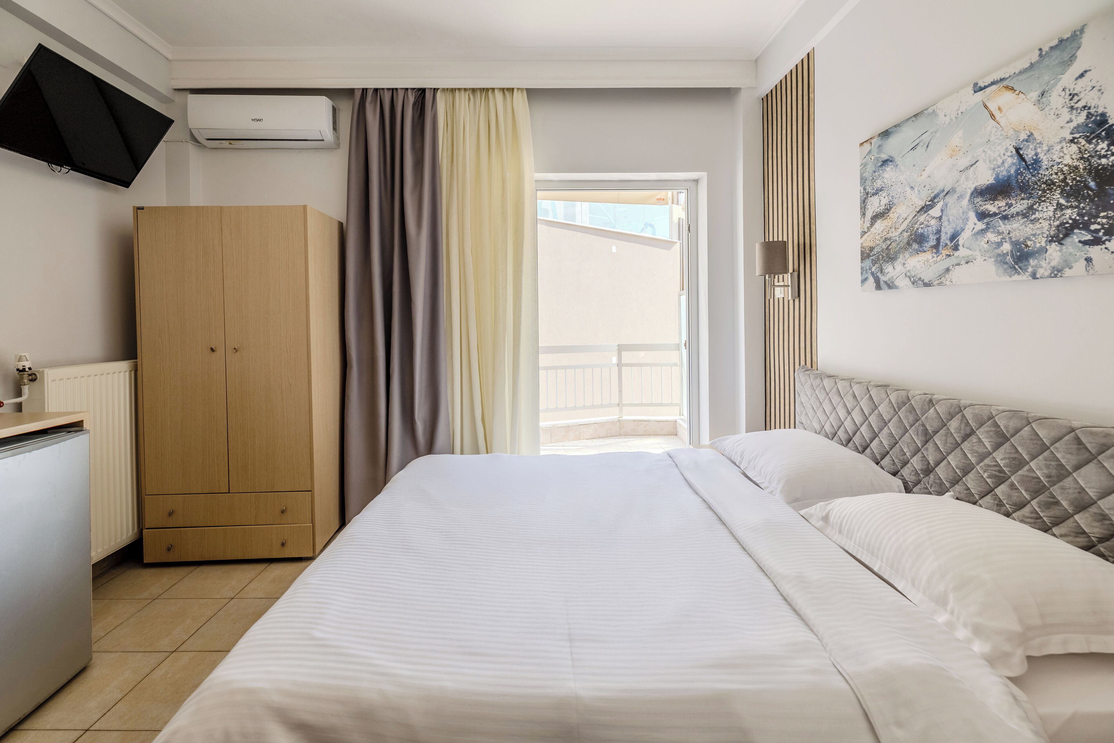 A hotel room with a bed, a wardrobe, a television, and a painting on the wall.