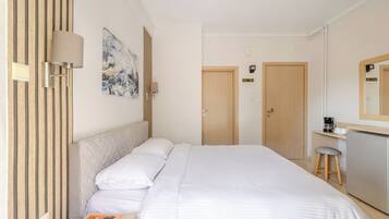 A hotel room with a bed, a desk with a chair, a coffee machine, and a mirror.