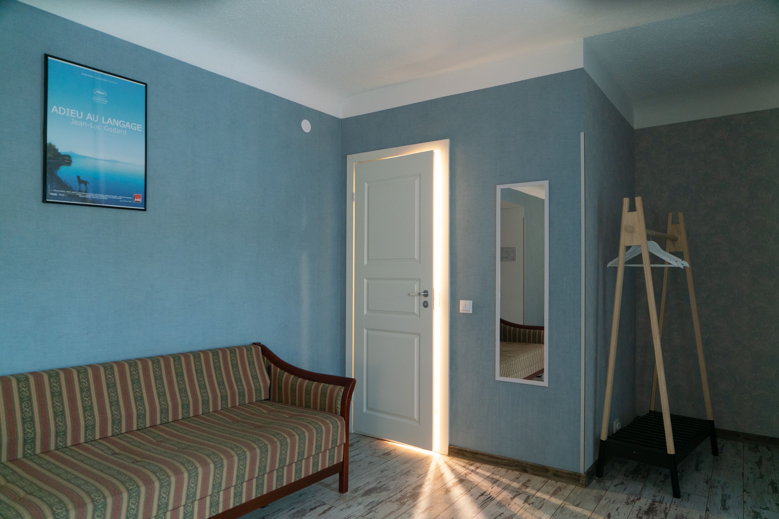 A room with a striped sofa, a door, a mirror, and a wooden easel.