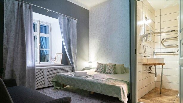 Un dormitorio con cama, ventana con cortinas, mesita de noche y baño con ducha.