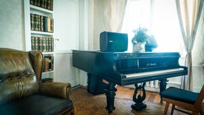 Un piano de cola en una habitación con suelo de madera, un sillón de cuero y una estantería llena de libros.