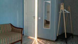 Una habitación con sofá de madera, una puerta blanca, un espejo y un perchero de madera.