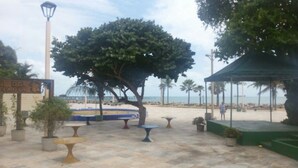 A paved outdoor area with tables and chairs, a large tree, and a sign with text. - Pousada do Castelo (Fortaleza)