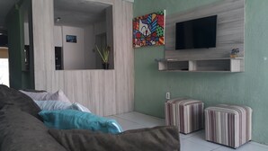 A living room with a sofa, ottomans, a TV, and a painting on the wall. - Pousada do Castelo (Fortaleza)