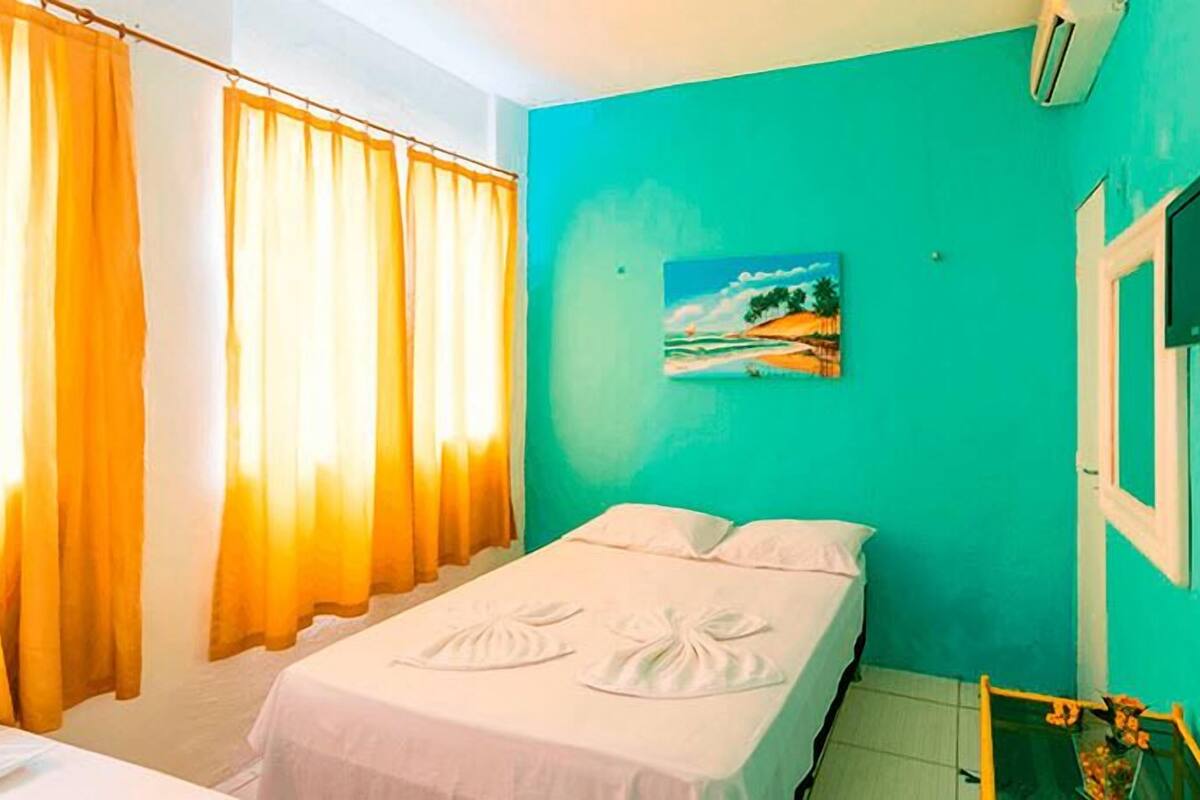 A room with a bed, curtains, a painting, and a TV.