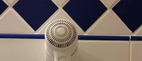 Un sèche-cheveux fixé au mur, avec une prise de courant et un interrupteur.