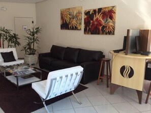 A living room with a black sofa, a white armchair, a coffee table with magazines, and two paintings on the wall. - Hotel Brisa Rio (Jacarei)