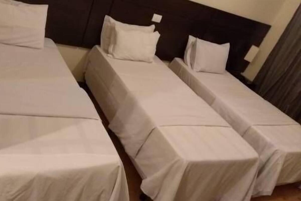 A hotel room with three single beds, each with a white bedspread and pillows.