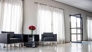 A modern, spacious room with two black leather chairs, a small table with a vase of red flowers, and a large window with white curtains. - Hotel Brisa Rio (Jacarei)