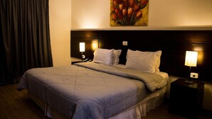 A hotel room with a large bed, two bedside lamps, a painting of tulips on the wall, and a dark headboard. - Hotel Brisa Rio (Jacarei)
