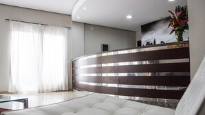 A modern hotel lobby with a white sofa, a reception desk, and a cityscape mural on the wall. - Hotel Brisa Rio (Jacarei)
