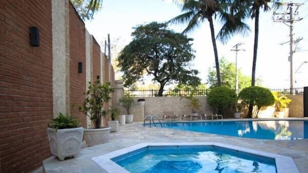 A swimming pool with a stone border, surrounded by a brick wall and palm trees. - Hotel Brisa Rio (Jacarei)