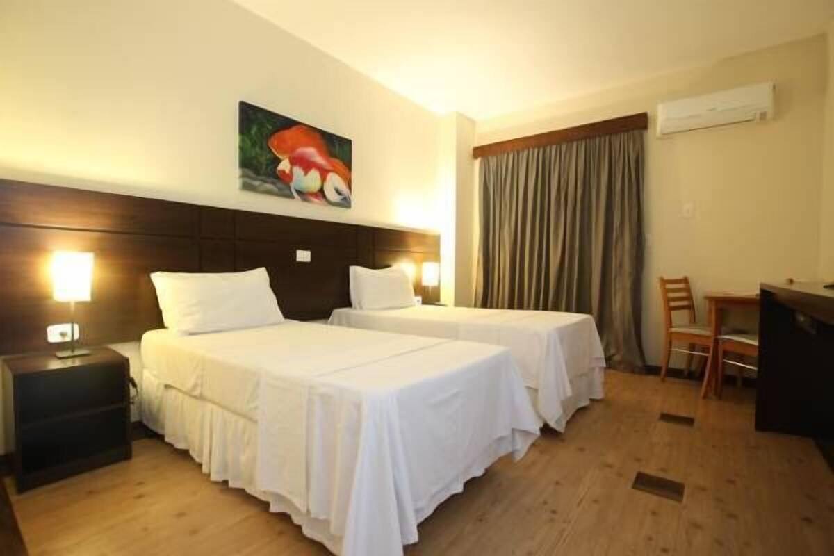 A hotel room with two beds, a desk, a chair, and an air conditioning unit.