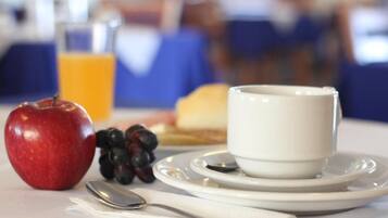 Et morgenbord med et rødt æble, druer, en hvid kop, et glas appelsinjuice og en tallerken med ristet brød og en ske på et bord.