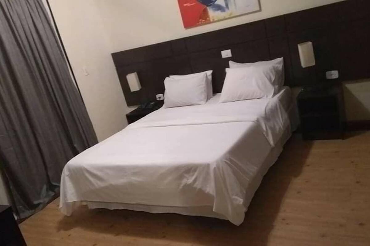 A neatly made bed with white linens in a room with a wooden floor and a dark headboard.