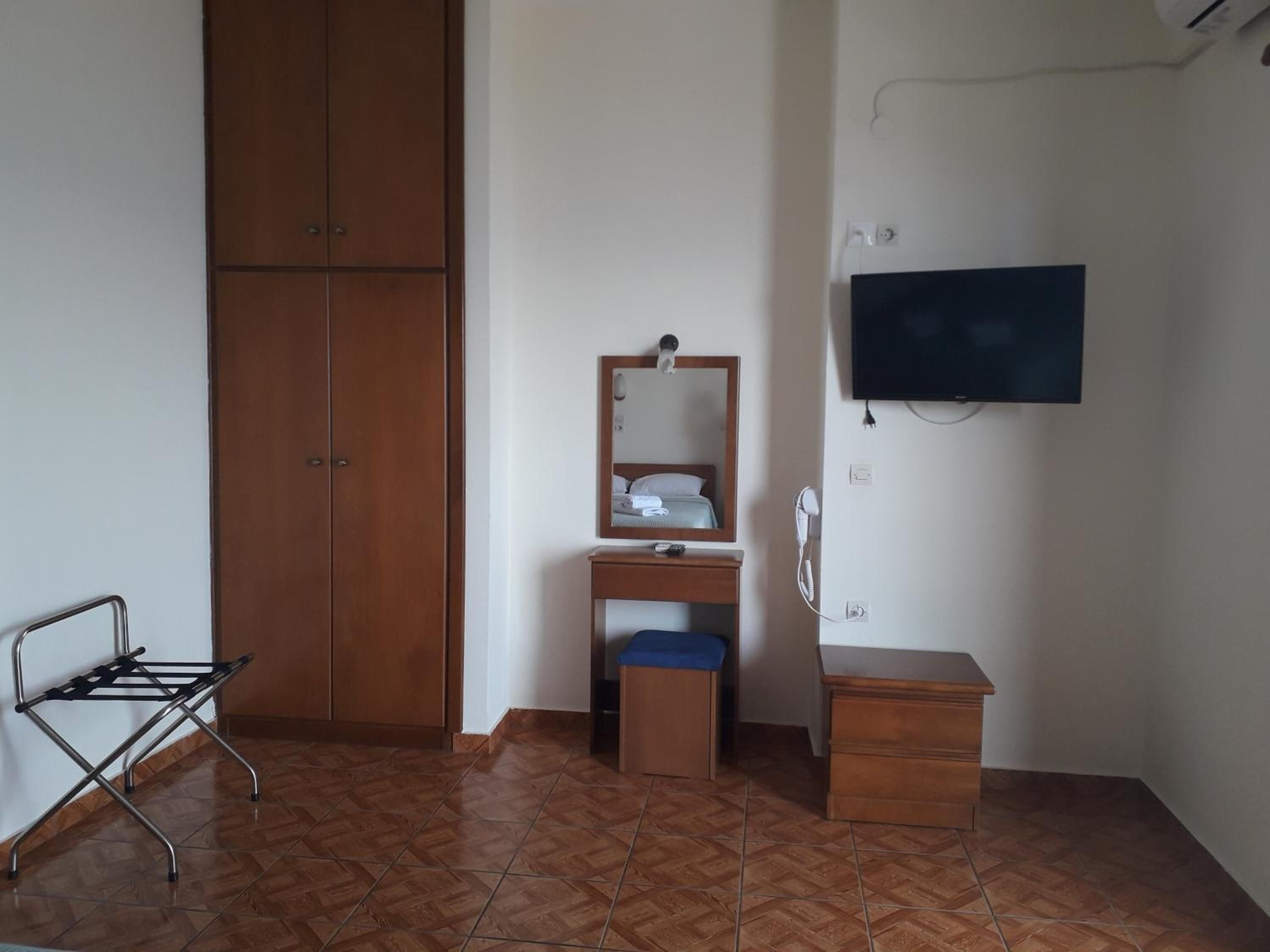 A room with a wardrobe, a vanity with a mirror, a television, and a small table.