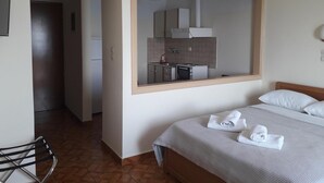 A hotel room with a bed, a chair, a view of the kitchen through a window, and a door leading to another room. - Hotel Poseidon (Chalcis)