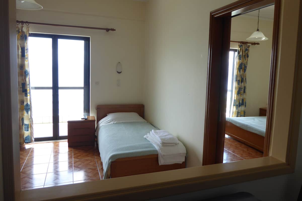 Un dormitorio con cama, mesita de noche, espejo y ventana con cortinas.