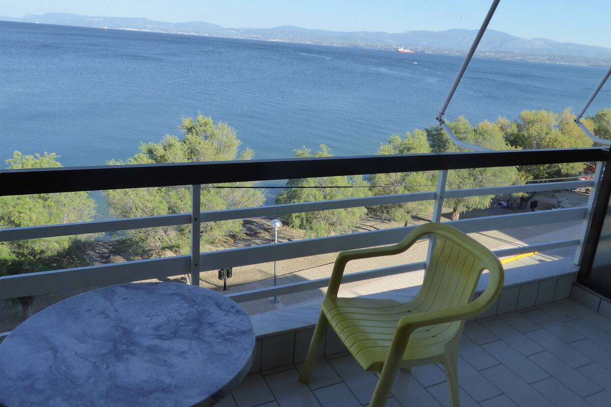 Un balcón con vista al mar, una silla amarilla y una mesita.