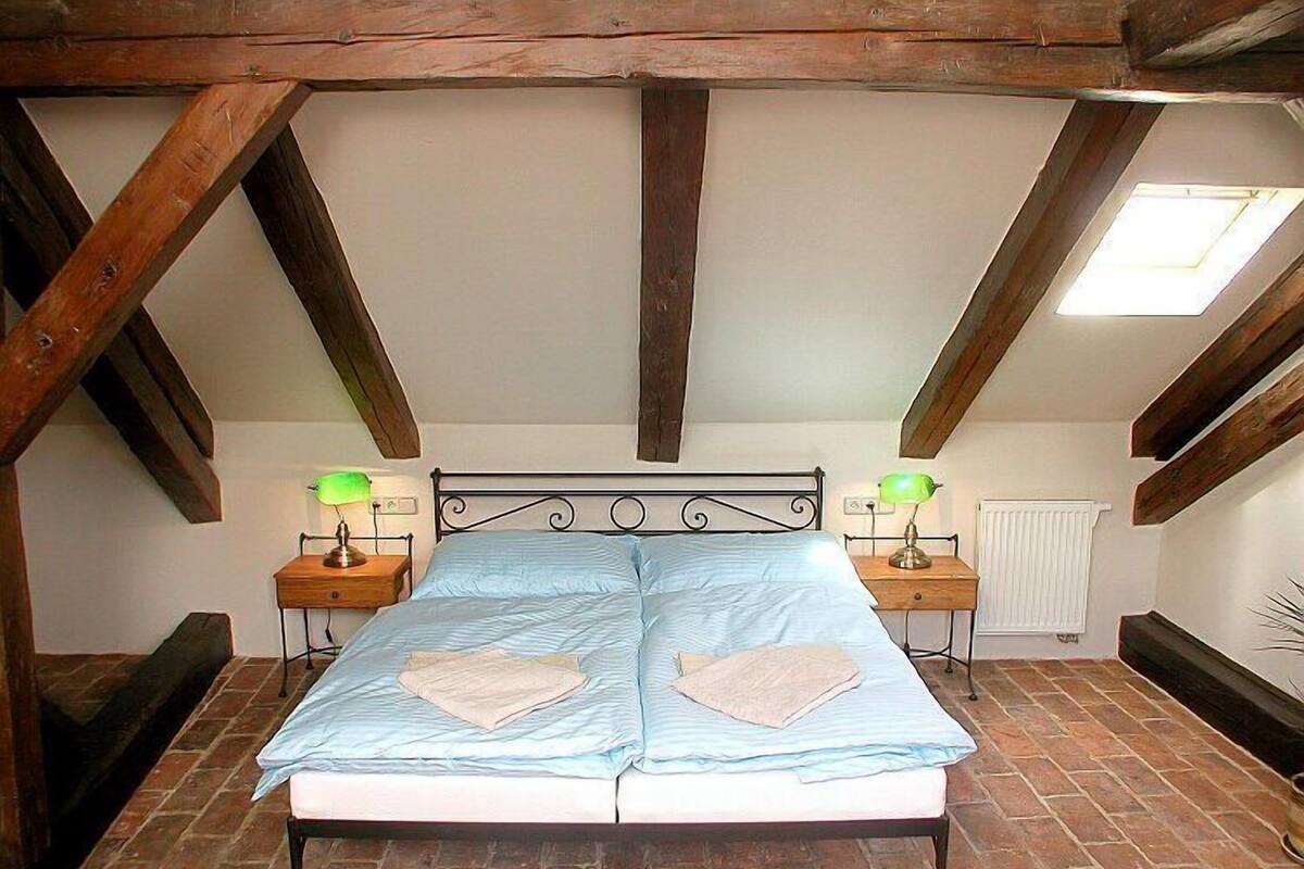A bedroom with a large bed, two bedside tables with lamps, a skylight, and exposed wooden beams.