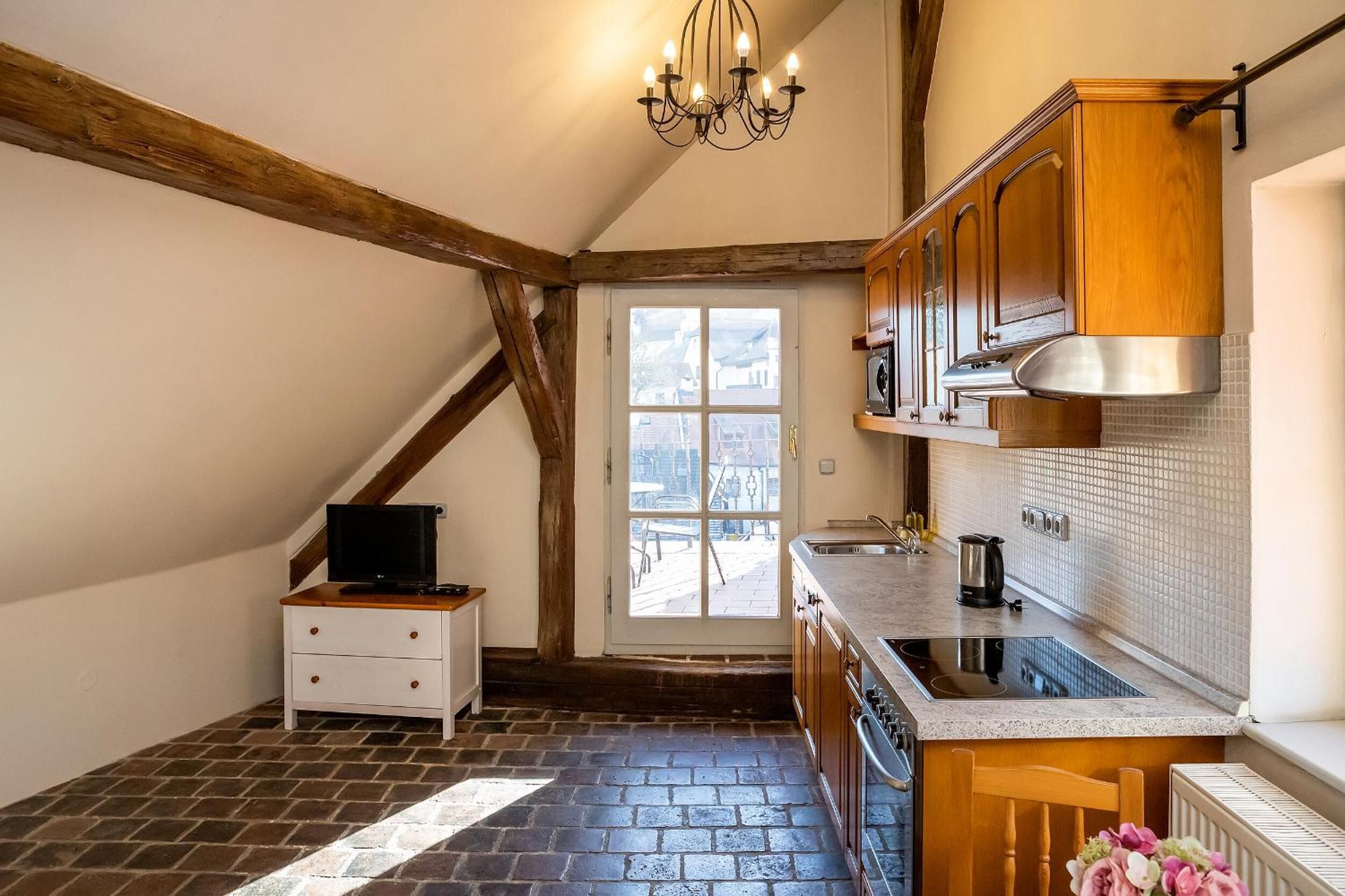 Una cocina con vigas de madera a la vista, estufa empotrada y ventana con vista a la calle.