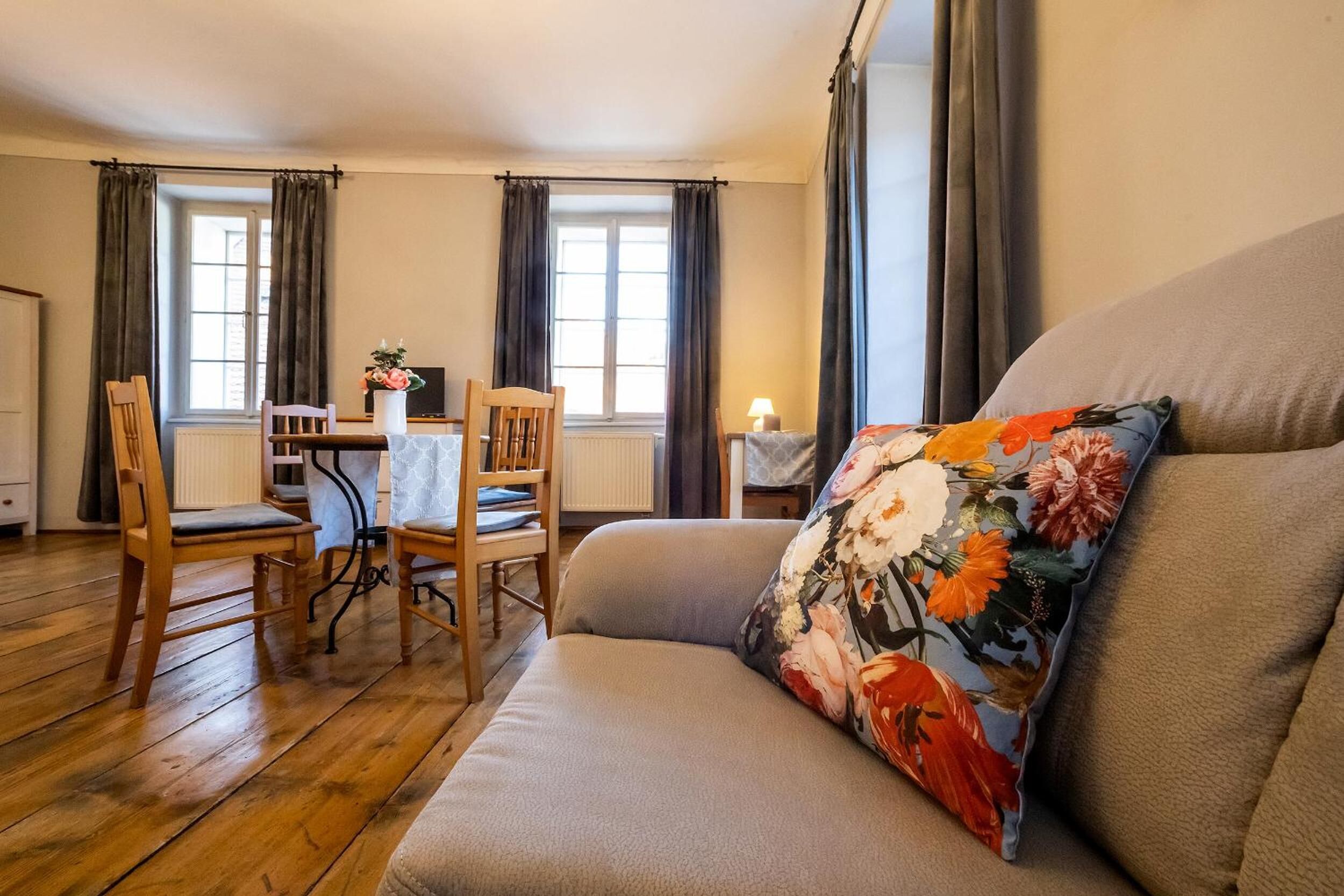 A cozy living room with a sofa, wooden chairs, a dining table, and a TV.