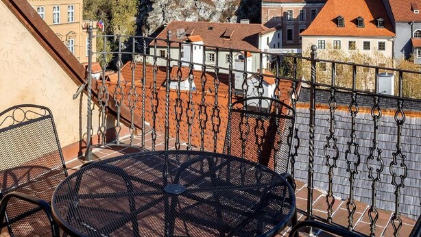 Una terraza con una mesa y sillas metálicas redondas, con vista a un edificio histórico con una torre y edificios de tejados rojos al fondo.