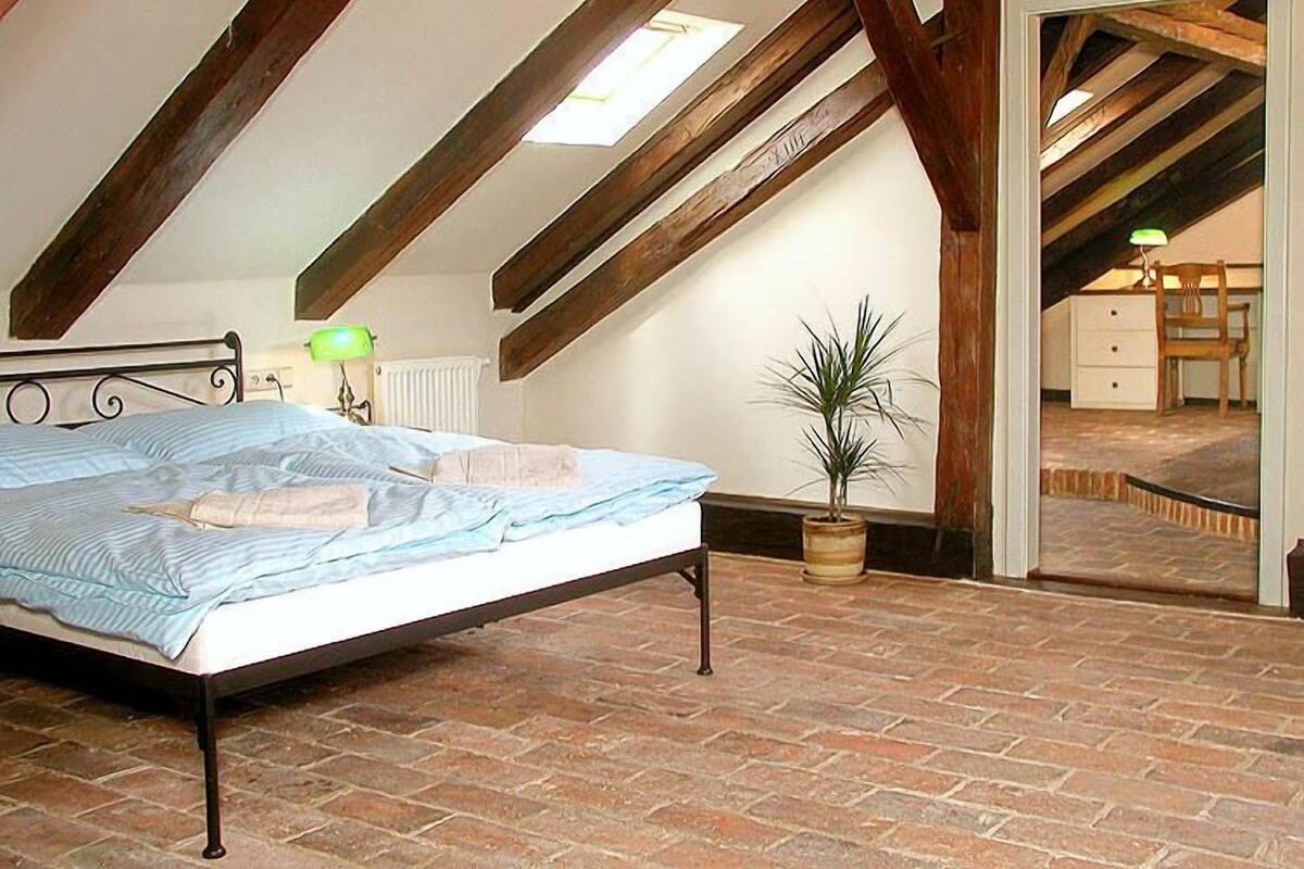 A bedroom with a brick floor, a bed with a metal frame, a potted plant, and a skylight.