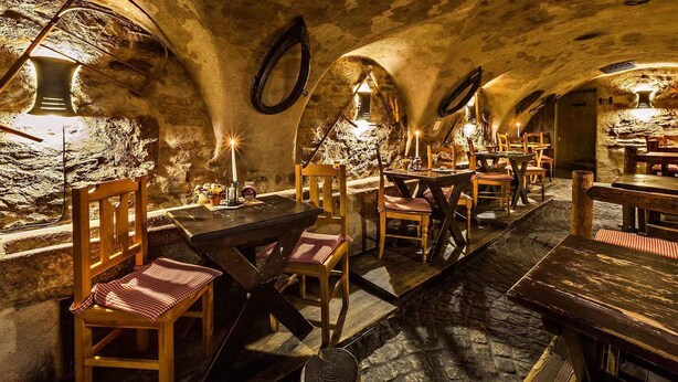 Un comedor rústico subterráneo con paredes de piedra, mesas y sillas de madera.