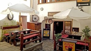 Un espacio de estar al aire libre con bancos y mesas de madera, un letrero que dice 'Mastal Penzion' y un menú de 'Beef Steaks'.