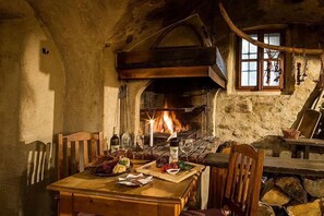 Un comedor rústico con una mesa de madera dispuesta para una comida, una chimenea de piedra y una ventana con vistas al exterior.