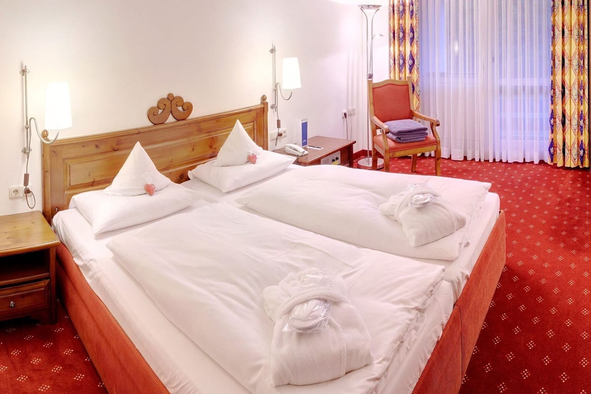 Ett hotellrum med en dubbelsäng, två sängbord, en stol och ett fönster med gardiner.