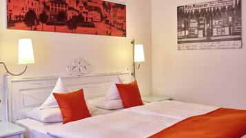 A hotel room with a bed, two bedside lamps, a headboard, and two paintings on the wall.