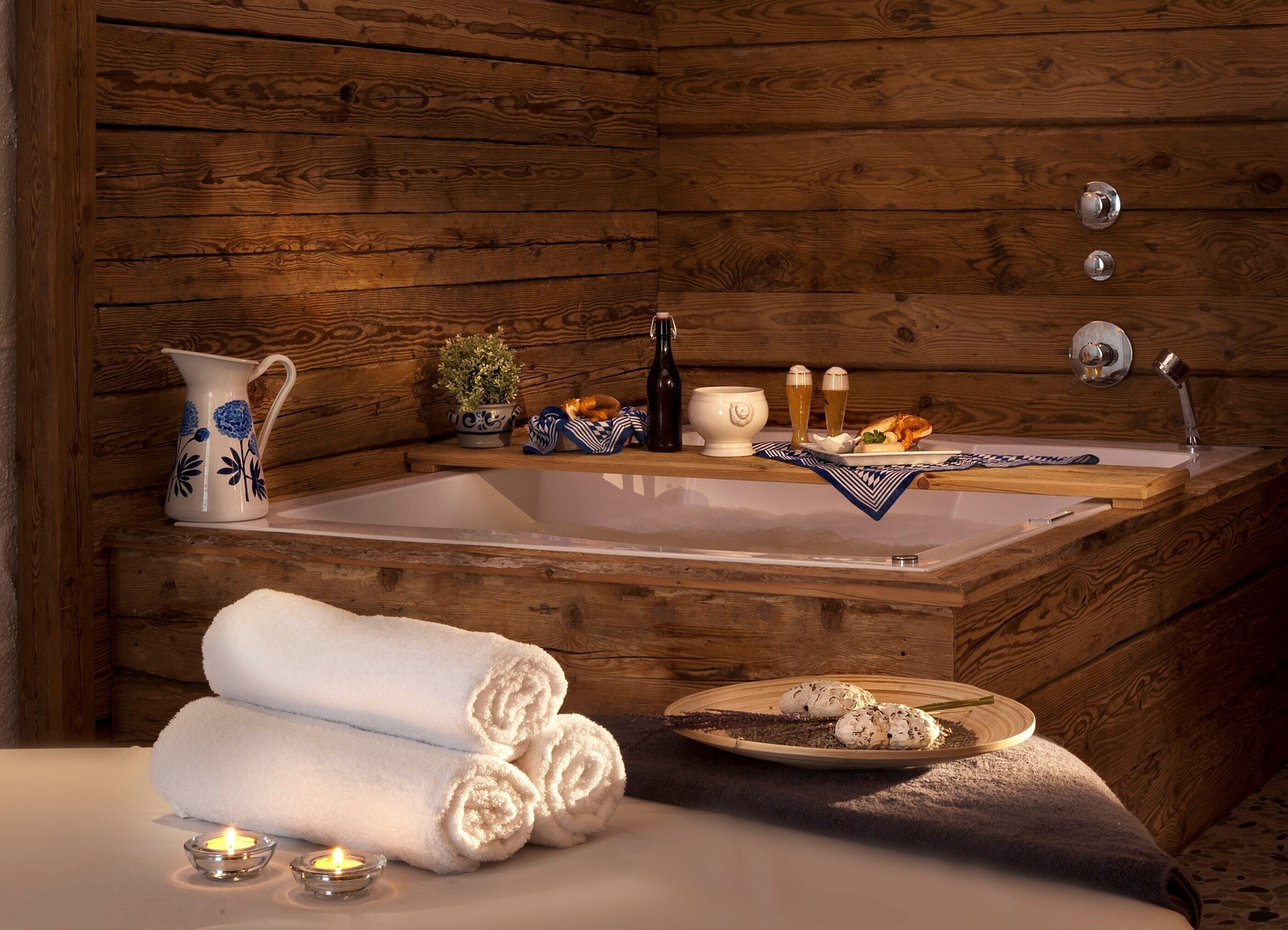 Interior de una cabaña de madera con bañera, toallas, velas y un plato de galletas.
