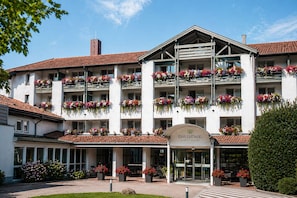 A multi-story building with balconies adorned with flowers, a sign reading 'Das Ludwig Sports Resort,' and a well-maintained outdoor area with potted plants. - DAS LUDWIG Sports Resort (Bad Griesbach im Rottal)