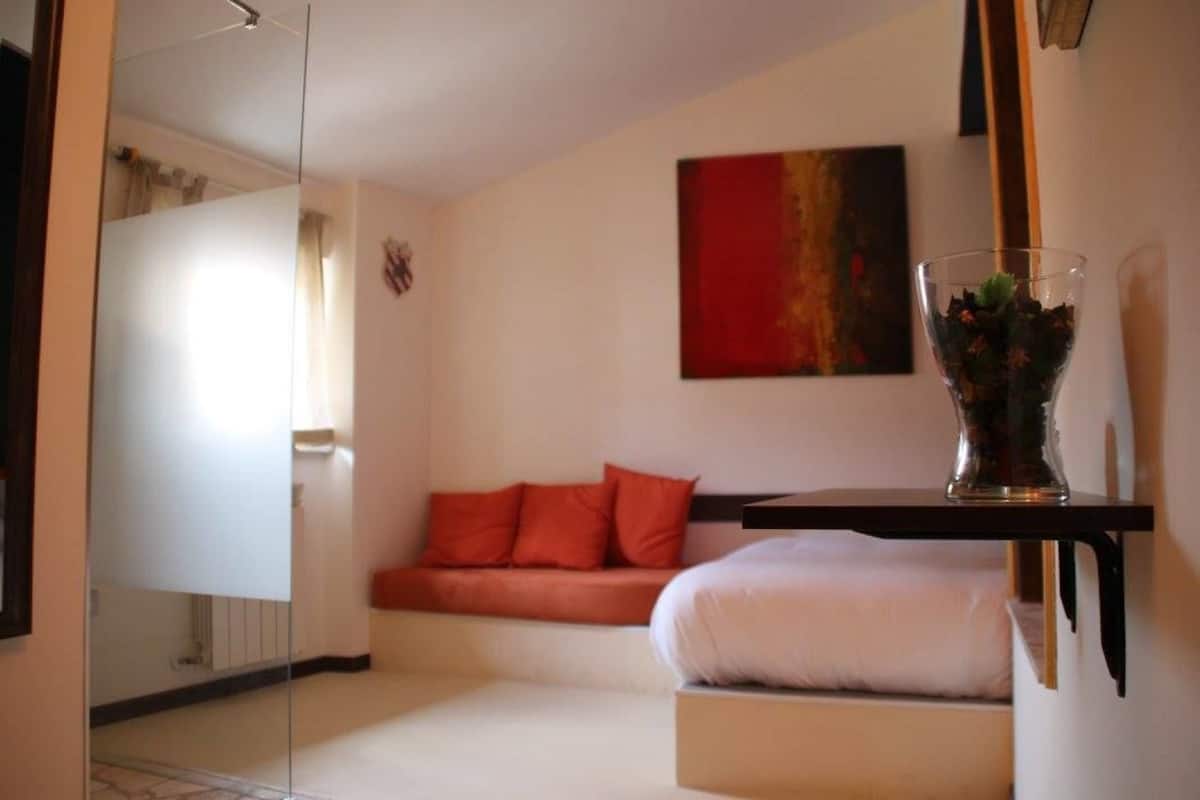 Ein modernes Schlafzimmer mit einer Glastrennwand, einem roten Sofa, einem weißen Bett und einem roten, abstrakten Gemälde an der Wand.