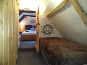 Ein schmaler Flur führt zu einem Schlafzimmer mit einem hölzernen Bett, einer Schiffslenken-Dekoration und einem Schild mit der Aufschrift 'Achtung, tiefer Durchgang'.