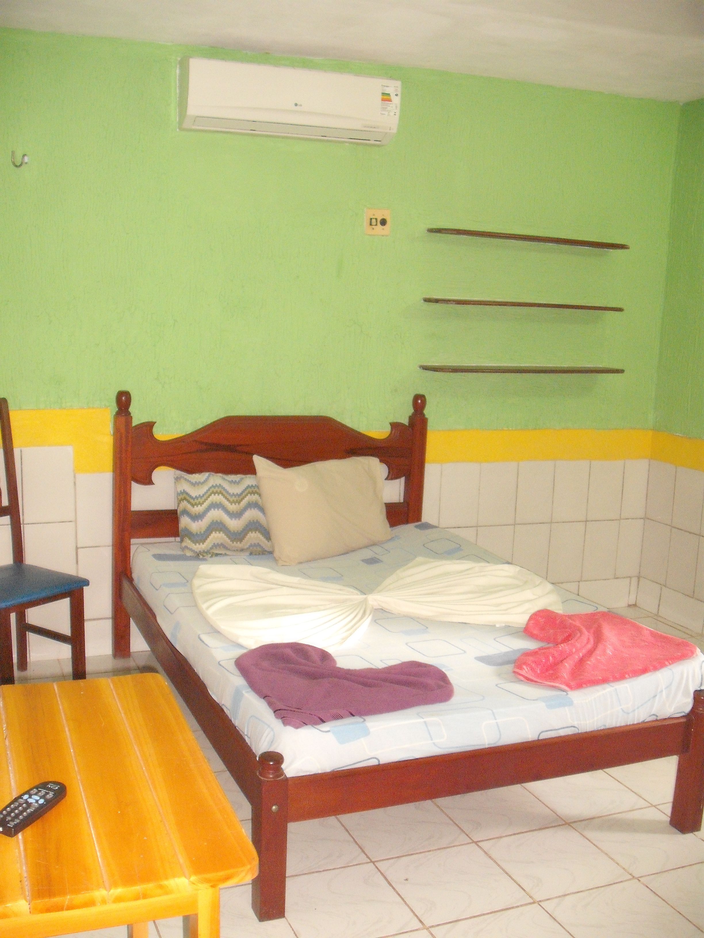 Una cama individual con cabecera de madera, una mesita de noche con control remoto y un aire acondicionado instalado en la pared.