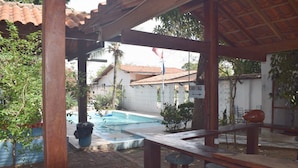 A covered outdoor area with a pool, wooden furniture, and a sign reading "CHUVEIRO". - Pousada Chalé Suiço (Parnaíba)