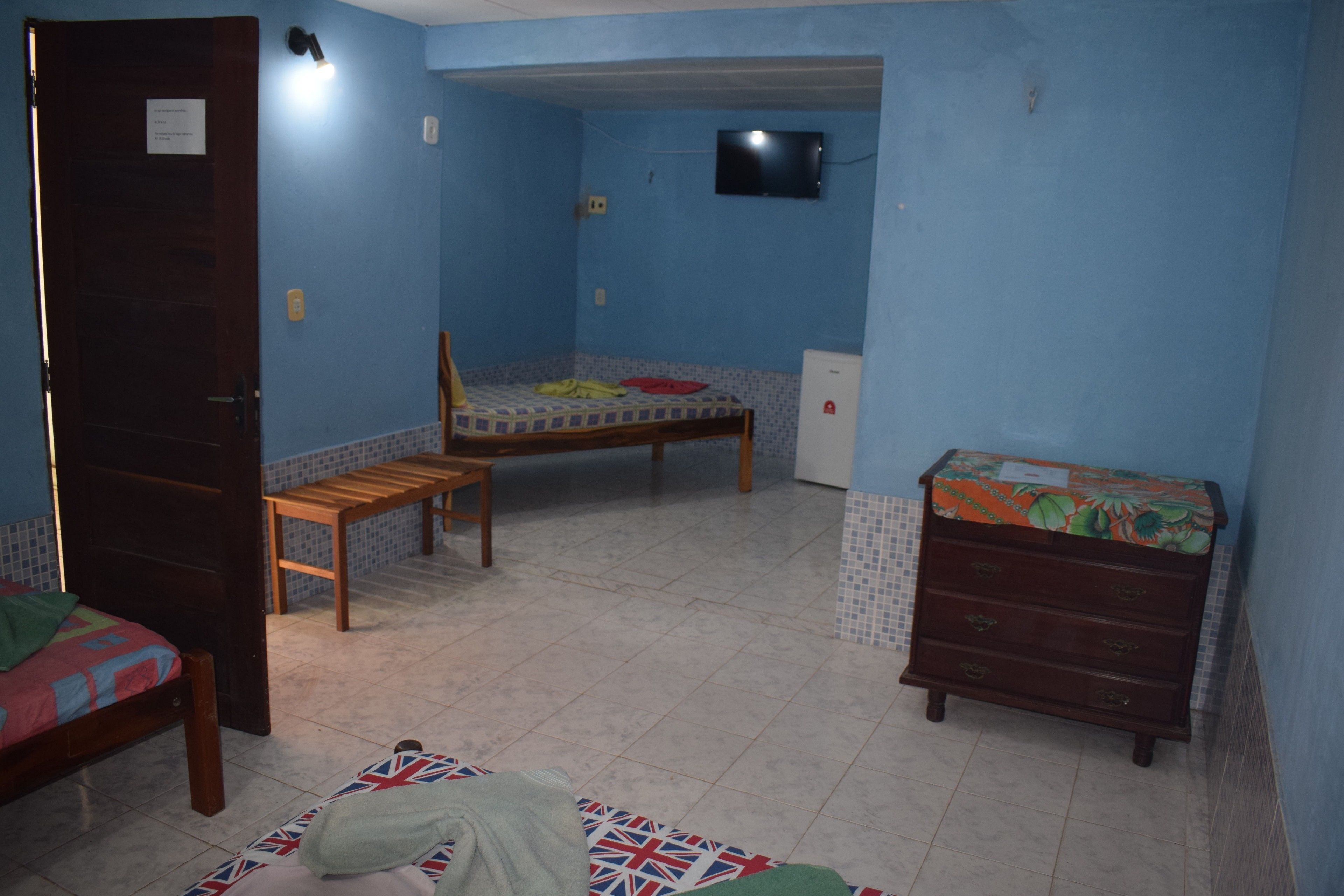 Un dormitorio con dos camas, una silla de madera, un aparador y un televisor en la pared.