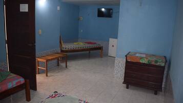Un dormitorio con dos camas, una silla de madera, un aparador y un televisor en la pared.