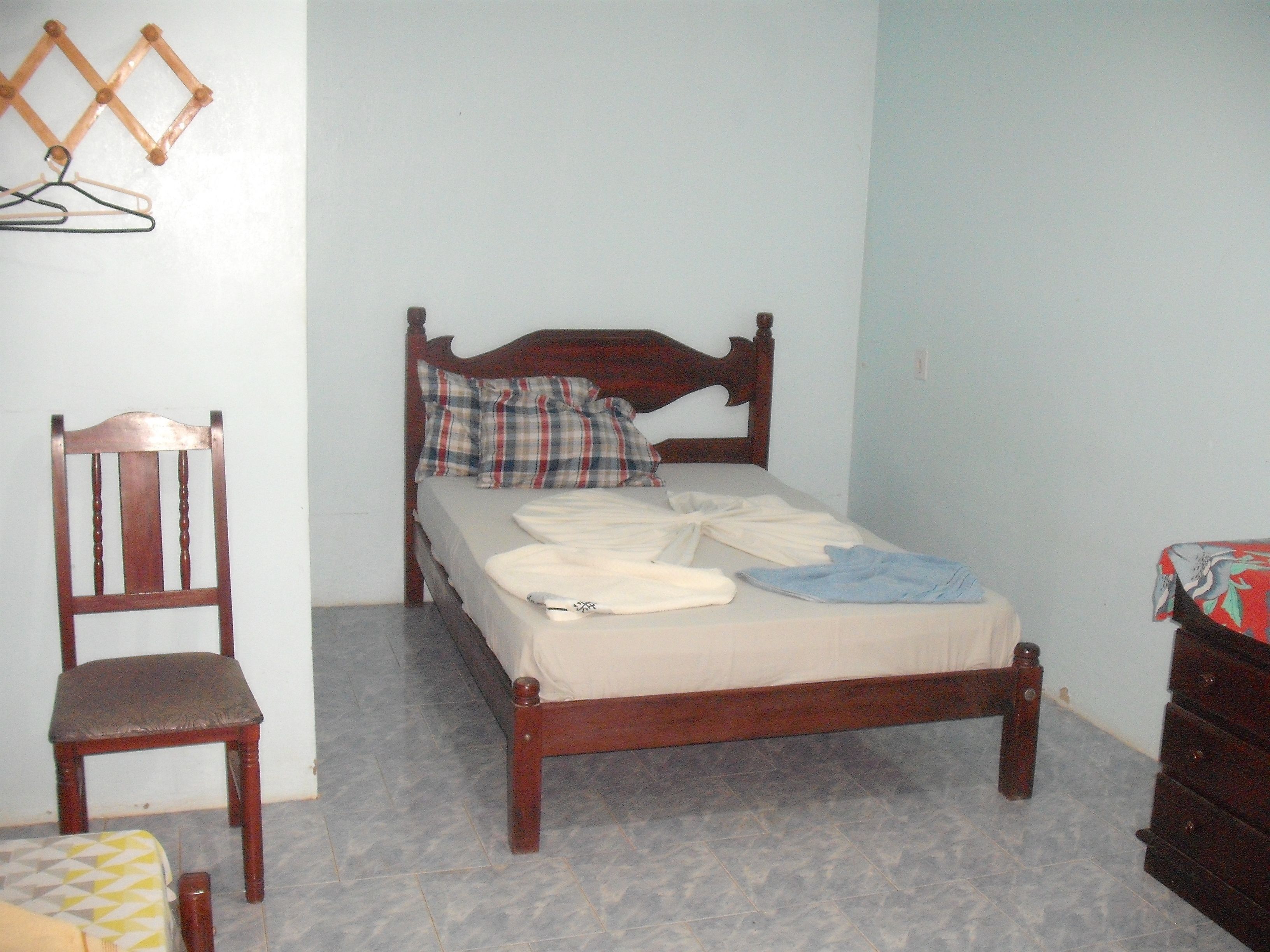Um quarto com uma cama de madeira, uma cadeira de madeira e um aparador.