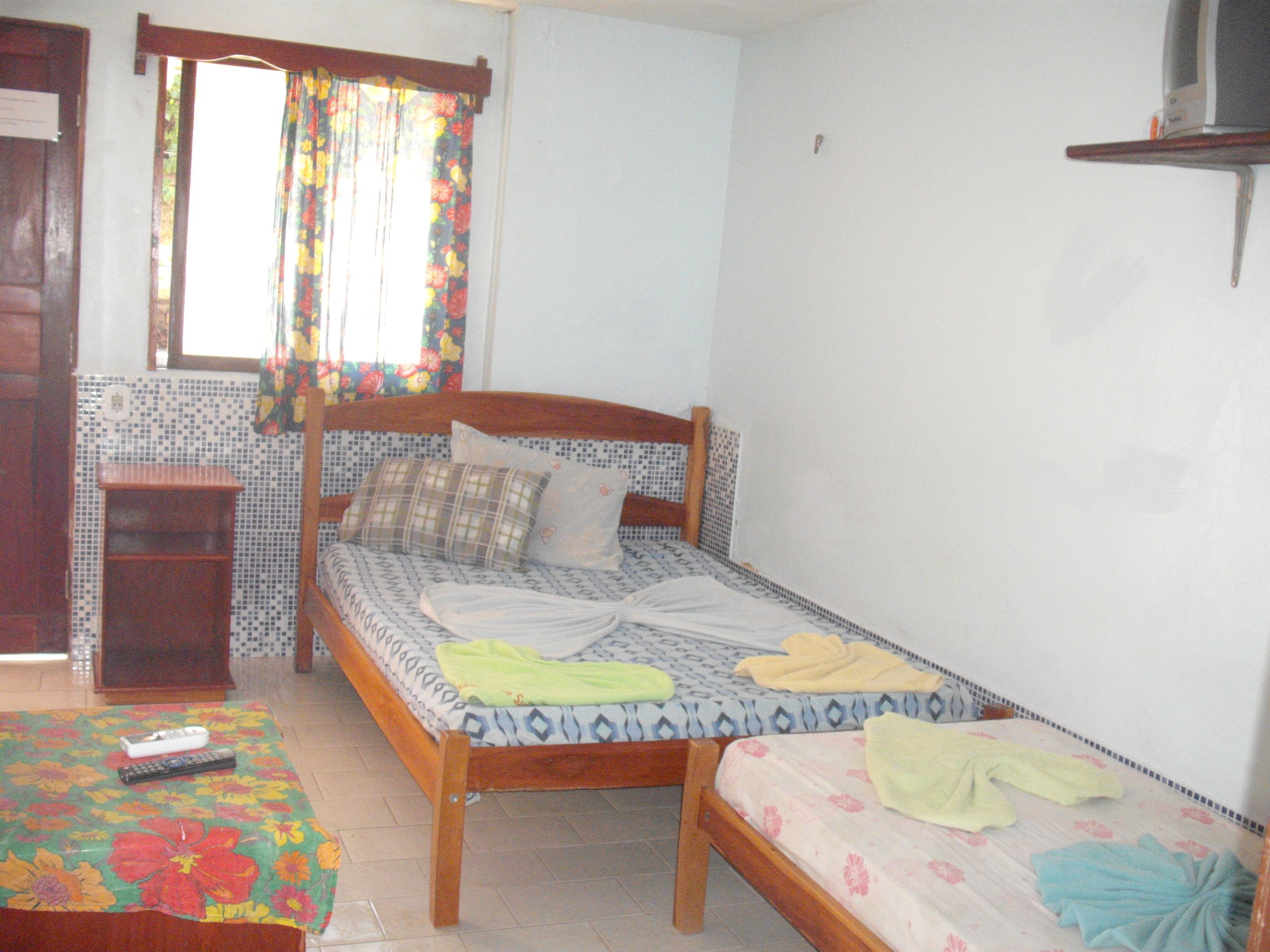A small, clean room with a single bed, a small table, and a window with curtains.