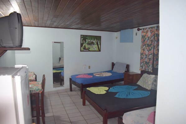 Una habitación pequeña y compacta con dos camas individuales, techo de madera, una mesita con una silla, un refrigerador y un cuadro en la pared.