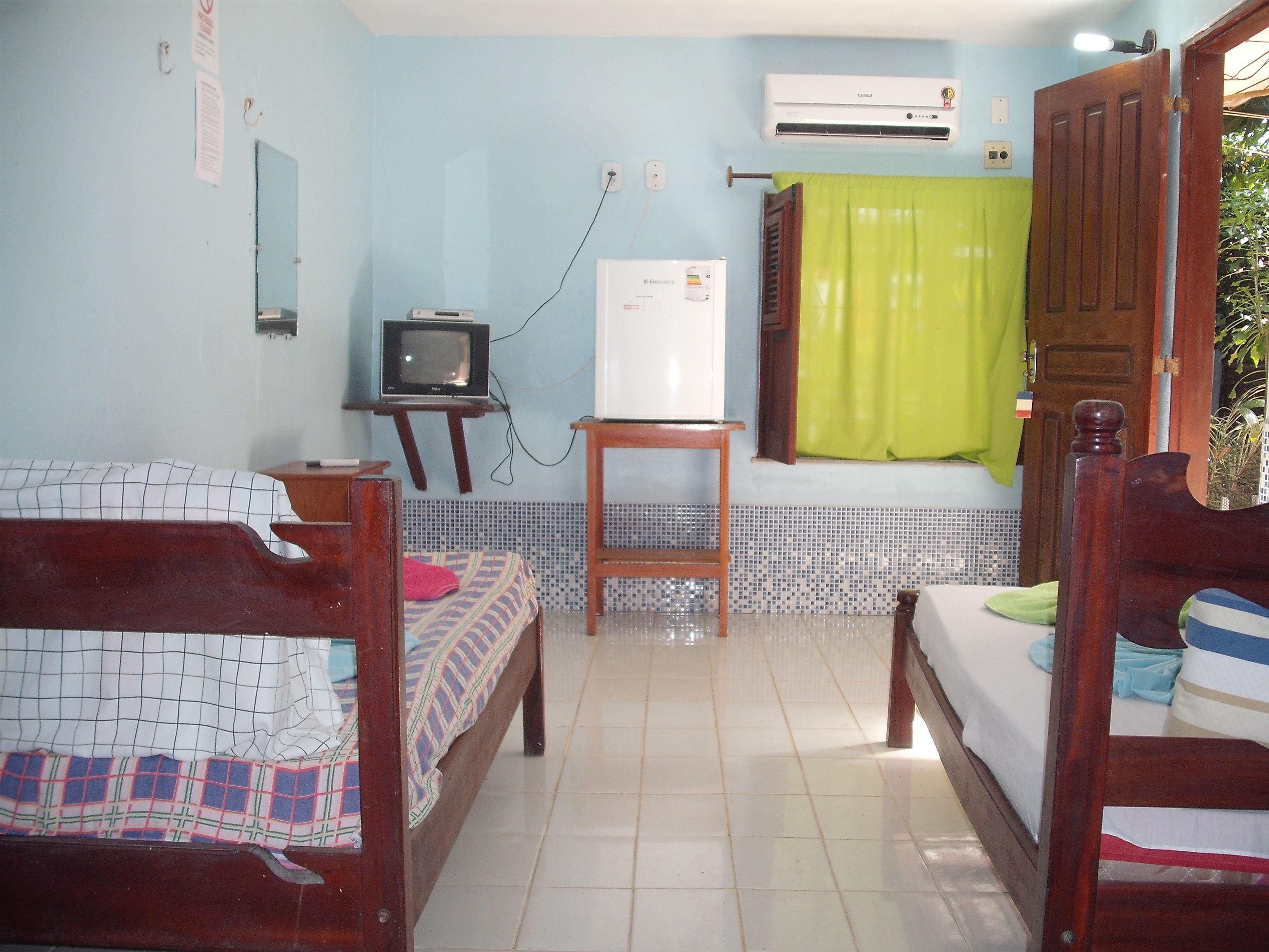 A room with two wooden beds, a small table, a television, and an air conditioner.