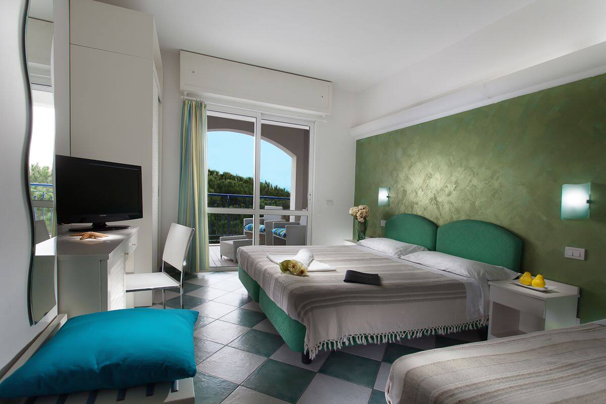 Habitación de hotel con cama, escritorio con televisor, silla, mesita de noche y vista al exterior.