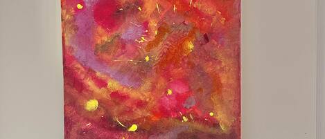 A square painting with abstract red and yellow colors on a white wall.