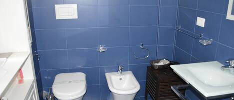 A bathroom with blue tiles, a toilet, a bidet, and a sink.