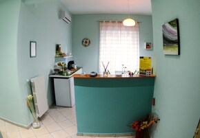 A kitchen with a teal countertop, a white radiator, a window with a curtain, and a small shelf with various items.